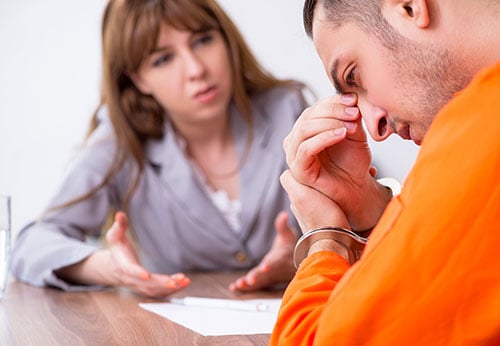 Felony defendant in orange jumpsuit consulting a lawyer in Baton Rouge, LA.
